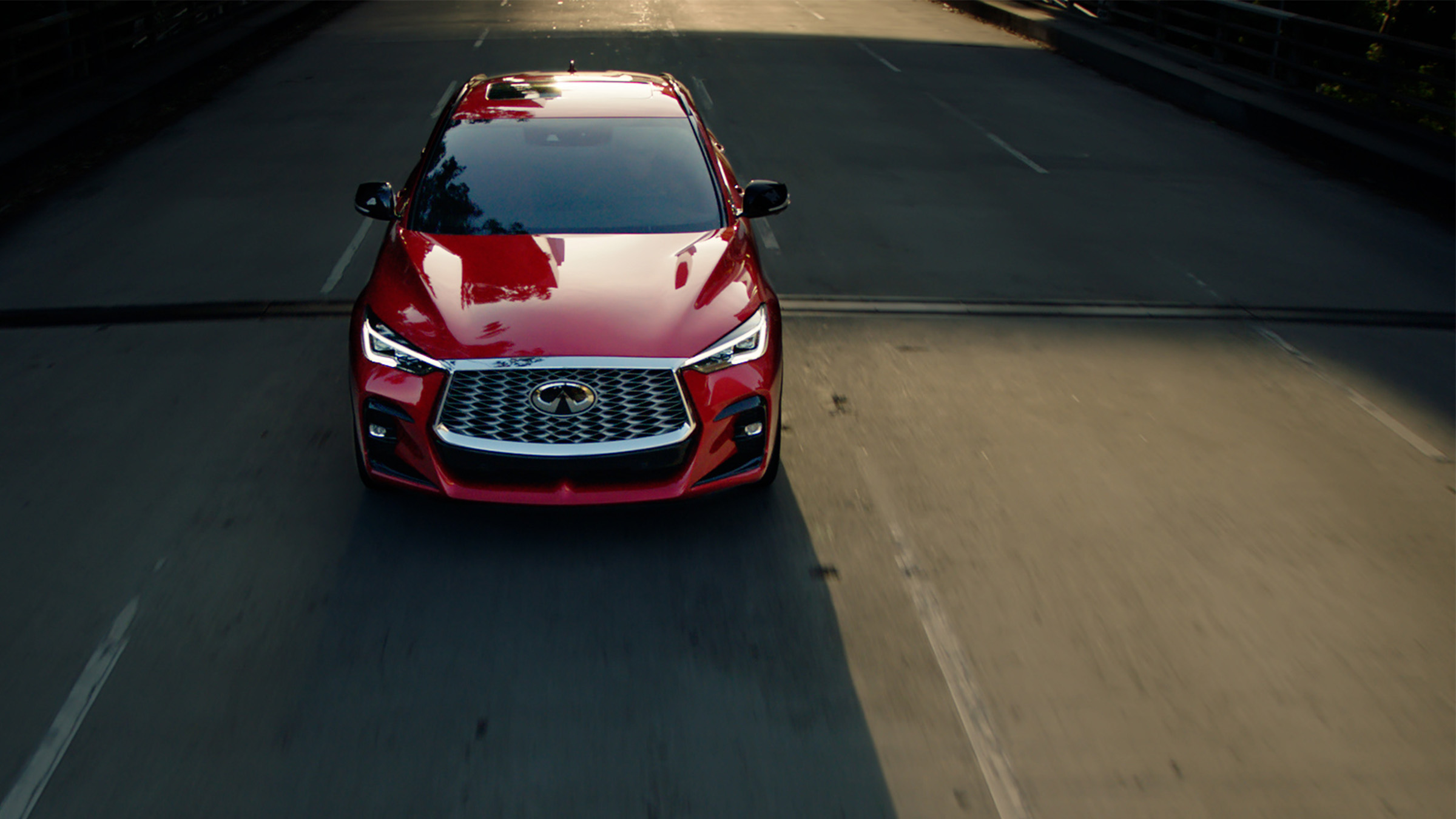 A red 2022 INFINITI QX55 crossover coupe driving down an empty road.
